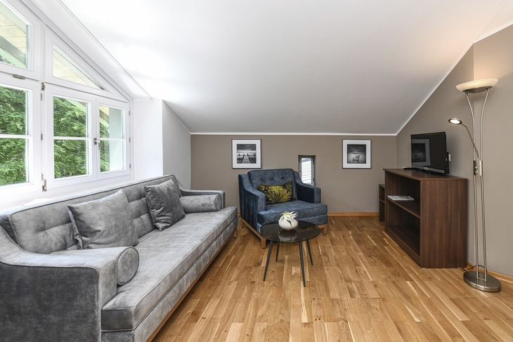 Wohnzimmer mit grauem Sofa, Sesseln und Fernseher auf Holzregal.