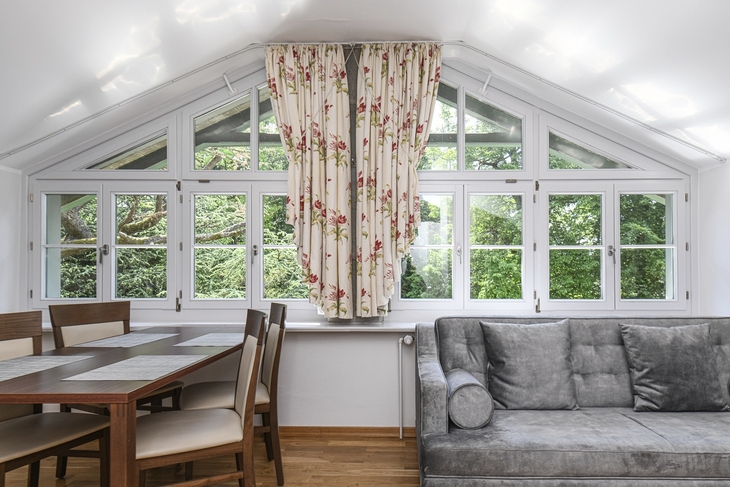 Wohnraum mit großem Fenster, Vorhängen, Couch und Esstisch.