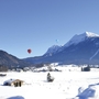Winterliche Alpenlandschaft mit Heißluftballons am Himmel.