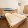 Schlafzimmer in der Ferienanlage Inzell, mit Holzfußboden, Doppelbett mit Nachttischen, Lampen und Bergpanoramabild am Kopfteil.