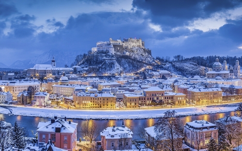 Blick auf das verschneite Salzburg mit Festung Hohensalzburg im Winter bei Abenddämmerung.