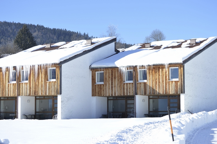 Verschneite Holzhäuser im Winter mit Eiszapfen am Dach.