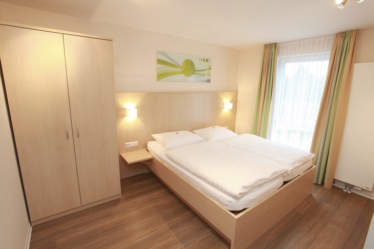 Helles Schlafzimmer mit Doppelbett, Kleiderschrank und Fenster.