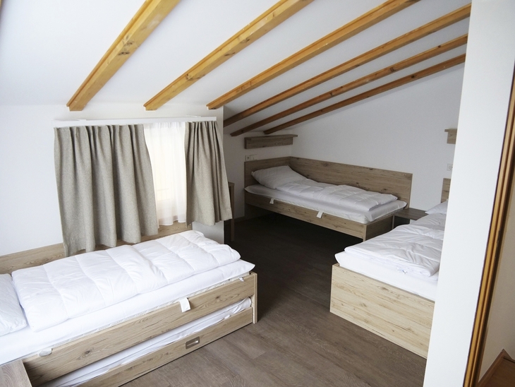 Schlafzimmer mit drei Einzelbetten, Holzbalkendecke und Vorhängen