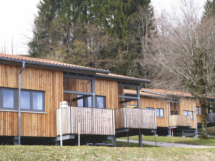 Reihenhäuser aus Holz mit Veranda in einer bewaldeten Umgebung.