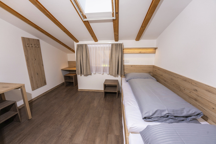 Helles Schlafzimmer mit zwei Einzelbetten, Holzverkleidung und Dachfenster.