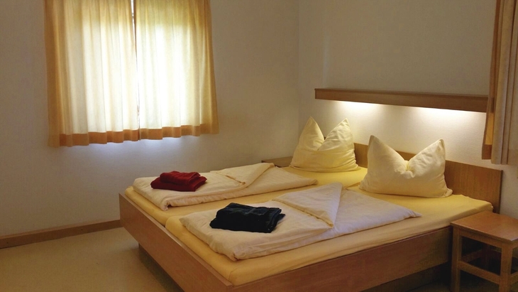 Doppelbett in einem gemütlichen Schlafzimmer mit Fenster und Vorhängen.