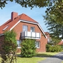Rotes Ferienhaus mit Garten und Balkon in Ferienanlage Harlesiel, umgeben von grünen Bäumen und einem Gehweg.