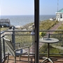 Blick vom Balkon, mit Tisch und Stuhl, der Ferienanlage Norderney auf das Meer. Rechts im Bild der achteckige weiße Pavillon mit grünem Dach.