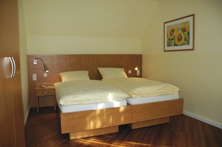 Schlafzimmer mit Doppelbett, Nachttisch und Sonnenblumenbild an der Wand in Ferienanlage Harlesiel.