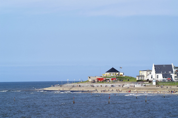 Küstenlandschaft mit Strand, Häusern und blauem Himmel.