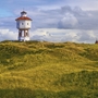 Leuchtturm auf der Insel Langeoog, umgeben von grasbedeckten Dünen unter wolkigem Himmel.