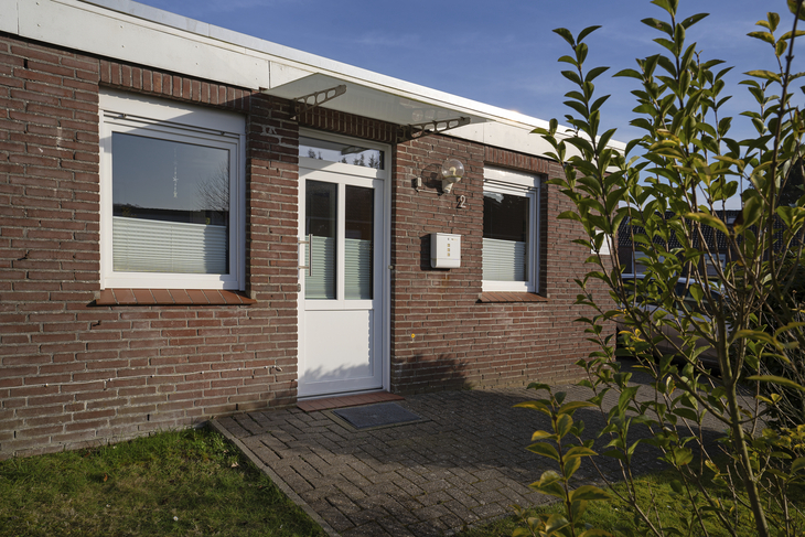 Backsteinferienhaus mit weißer Tür und Fenstern, umgeben von Grün.