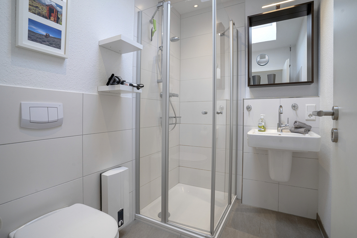 Modernes Badezimmer mit Dusche, Waschbecken, Toilette und Spiegel.