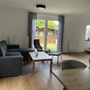 Wohnzimmer mit grauem Sofa, Holztisch und Blick auf den Garten im Ferienhaus.