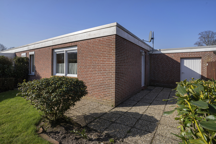 Backsteinhaus mit Garten und Terrasse unter blauem Himmel.