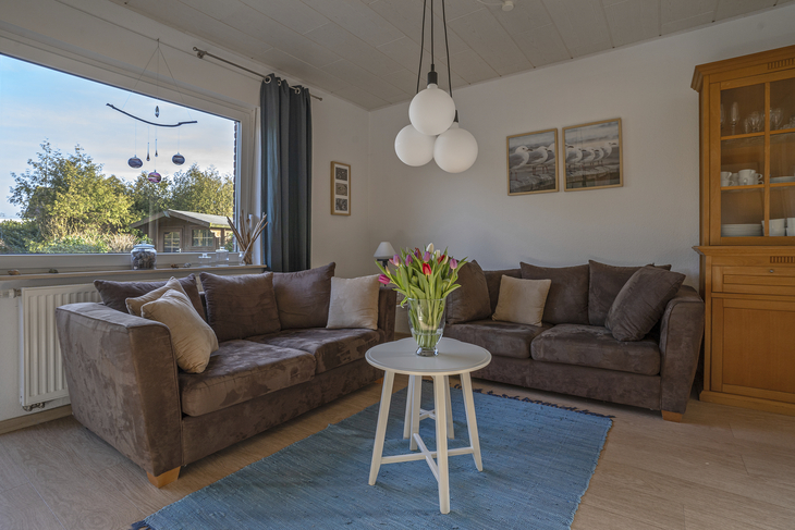 Wohnzimmer mit braunen Sofas, Couchtisch und großen Fenstern.