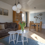 Wohnzimmer mit Sofa, zwei Tischen, Blumenstrauß, Esstisch und Stühlen in hellem Raum.