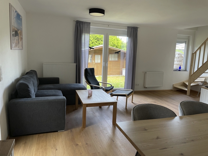 Wohnzimmer mit grauem Sofa, Holztisch und Blick auf den Garten im Ferienhaus.
