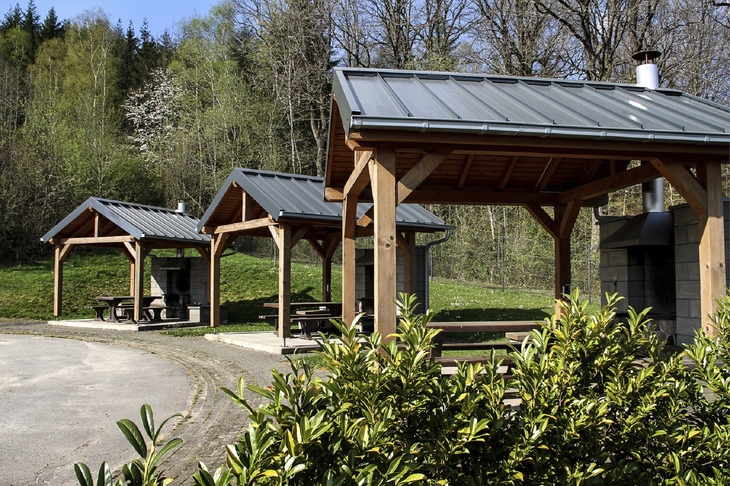 Drei einzelne jeweils überdachte Picknicktische in der Ferienanlage Prüm vor einem Waldgebiet.