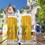 Zwei Gläser Kölschbier auf einem Holztisch vor bunten Häusern in Köln.