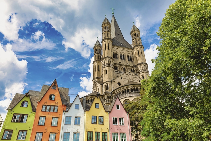 Groß St. Martin Kirche in Köln mit bunten Häusern im Vordergrund bei sonnigem Wetter.