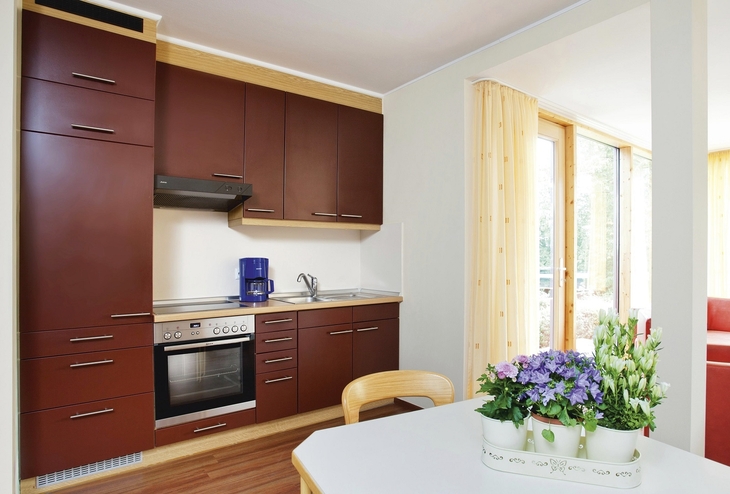 Dunkelrote Küche mit Esstisch und Blumenarrangement in der Ferienanlage Prüm.