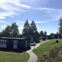 Mehrere kleine Gebäude in einer grünen Parklandschaft bei sonnigem Wetter.
