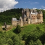 Burg Eltz inmitten grüner Hügellandschaft bei sonnigem Wetter.