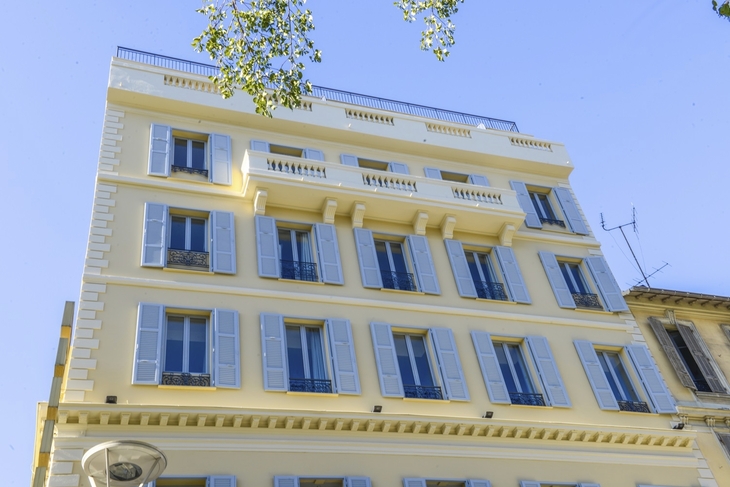 Fassade eines mehrstöckigen Gebäudes mit blauen Fensterläden und Balkonen.