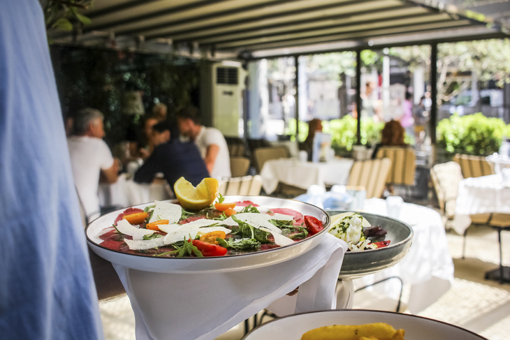 Gartenrestaurant mit gedeckten Tischen und serviertem Salat im Vordergrund.