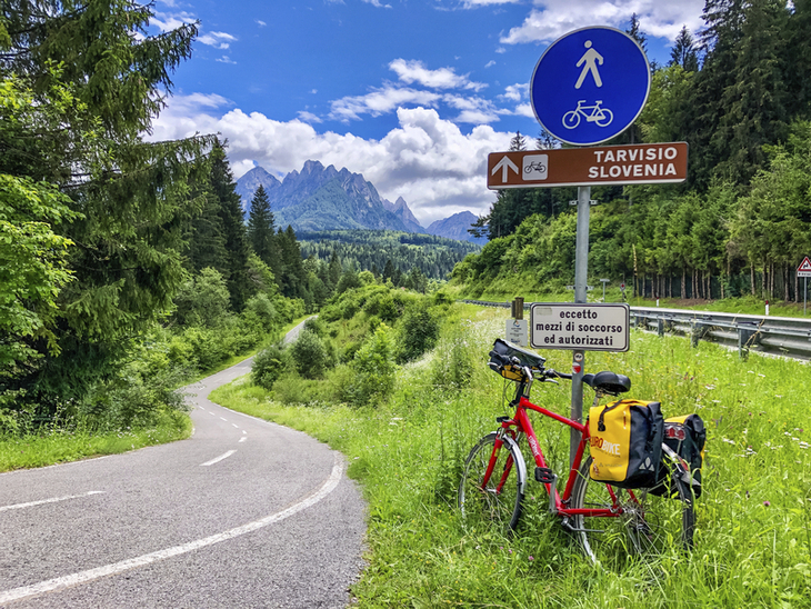 Wegweiser nach Tarvisio, Slowenien, nahe einem Radweg mit geparktem Fahrrad.