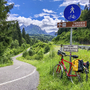 Wegweiser nach Tarvisio, Slowenien, nahe einem Radweg mit geparktem Fahrrad.