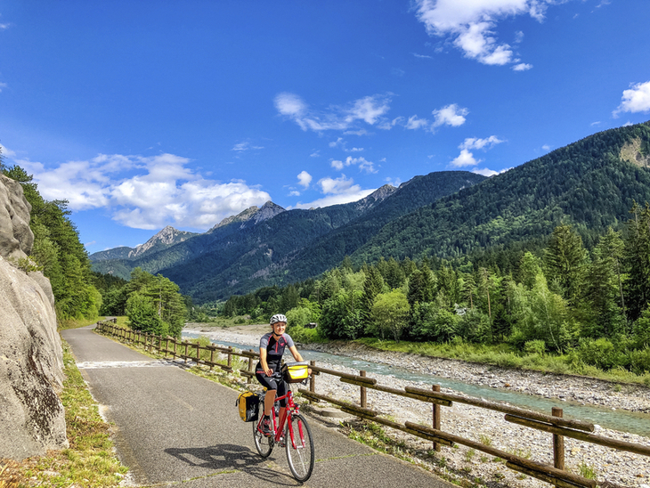 Radfahrer auf landschaftlichem Weg zwischen Bergen und Fluss.
