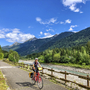 Radfahrer auf landschaftlichem Weg zwischen Bergen und Fluss.