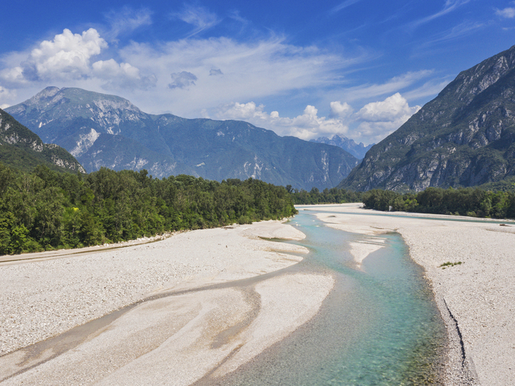 Blick auf einen breiten Fluss mit Bergen im Hintergrund an einem sonnigen Tag.