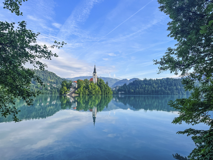 Kirche auf Insel im Bleder See, umgeben von Wasser und bewaldeten Hügeln.