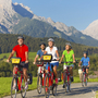 Radfahrergruppe auf einem Weg vor Berglandschaft im Sommer.