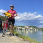 Fahrradfahrerin am Ufer eines Flusses mit Landschaft im Hintergrund auf dem Tauernradweg.