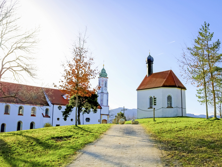 Kirche und Gebäude mit Alpen im Hintergrund bei klarem Himmel.