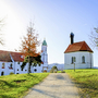Kirche und Gebäude mit Alpen im Hintergrund bei klarem Himmel.