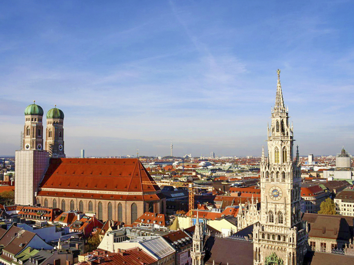 Blick auf Münchens Frauenkirche und Rathaus bei blauem Himmel.