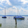 Boote schwimmen auf dem Starnberger See vor einer Alpenkulisse unter bewölktem Himmel.