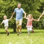 Familie läuft fröhlich im Park auf grüner Wiese.