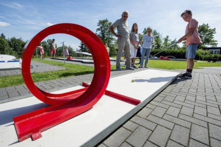 Kind spielt Minigolf mit Looping in der Ferienanlage Prüm. Ein anderes Kind und die Eltern schauen zu