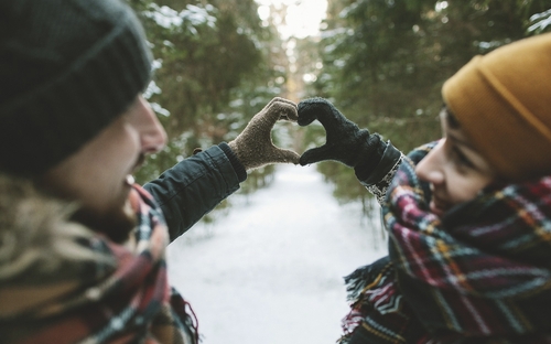 Ein Paar formt ein Herz mit Handschuhen im winterlichen Schwarzwald.