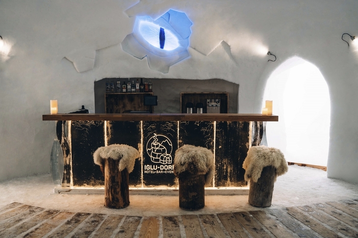 Innenansicht einer Schneebar im Iglu-Dorf mit Holzhockern und Theke.