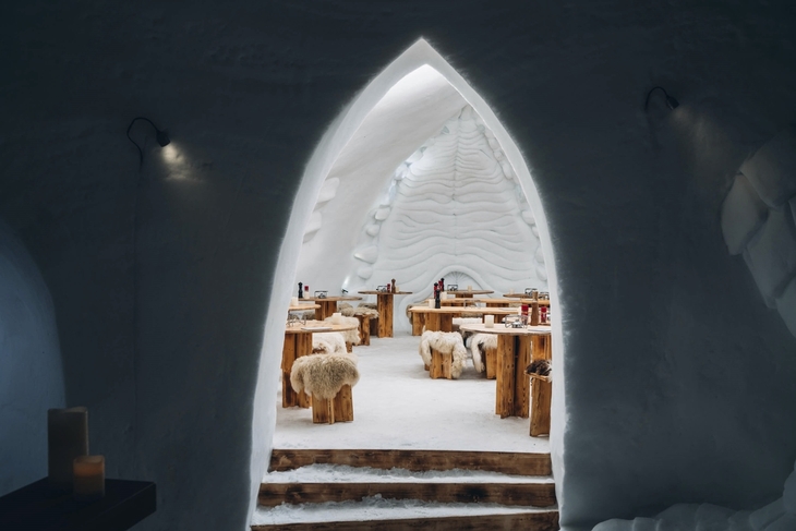 Eingang zu einem Iglu-Restaurant mit Holztischen und Fell bedeckten Stühlen.