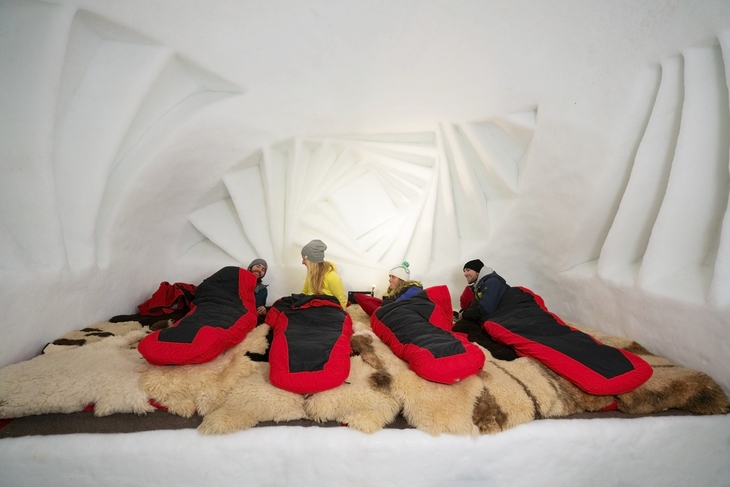 Personen in Schlafsäcken in einem dekorativen Iglu-Innenraum.