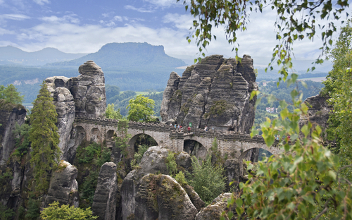 Blick auf die Basteibrücke im Elbsandsteingebirge mit umliegenden Felsen und Wald.